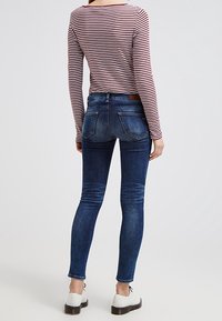 Jeans ajustados en denim oscuro con ligeros desgastes, combinados con una camiseta de manga larga a rayas. Zapatos blancos con suelas negras completan el conjunto.