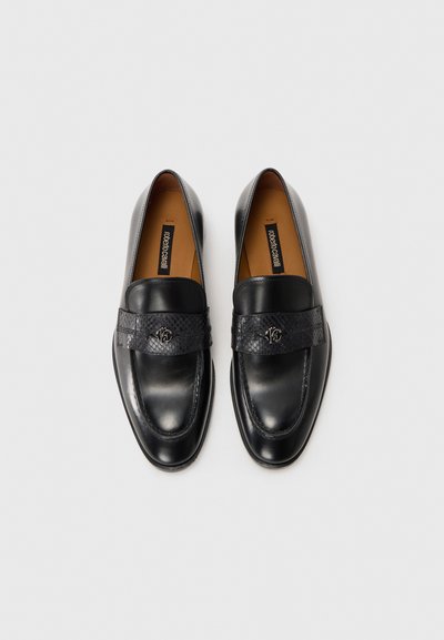 Ett par svarta läderloafers med band i snakeskin-textur och metallisk logotypdetalj på vit bakgrund.