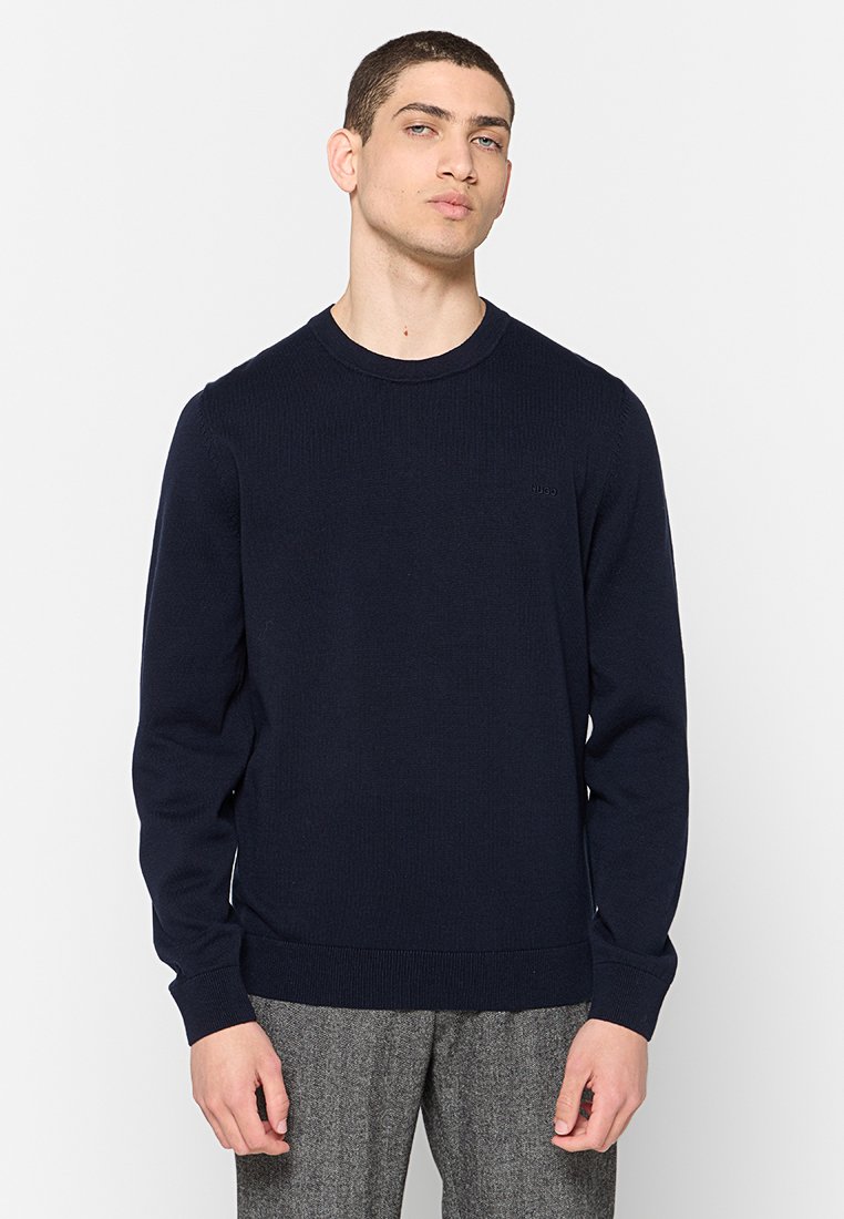 Pull en tricot bleu marine avec un col rond, texture côtelée et manches longues. Présente un détail de logo discret sur la poitrine.