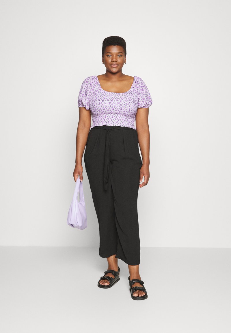 Blusa floral roxa de mangas curtas com decote quadrado, combinada com calças pretas ajustadas e uma bolsa lilás; sandálias pretas com tiras.