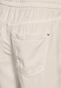 Pantalones de color beige claro con cinturilla elástica, que cuentan con dos bolsillos traseros y detalle de costura visible. Textura de tela suave.