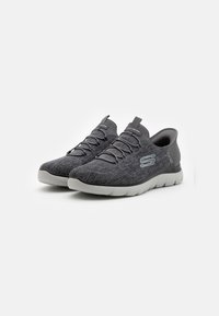 Zapatillas deportivas de punto gris con un patrón texturizado, que cuentan con cordones elásticos, una suela acolchada y un logo en el lateral.