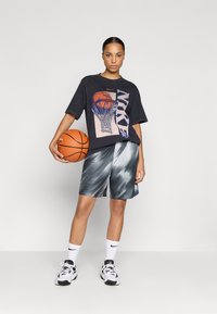 Tricou negru supradimensionat cu un grafic de baschet, pantaloni scurți gri cu un model, și adidași albi. Modelul ține o minge de baschet. Texturi netede.