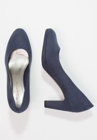 Scarpe col tacco alte di colore blu navy, con una texture scamosciata liscia, punta tondeggiante e tacco largo a blocco. Fodera di colore argento visibile all'interno.