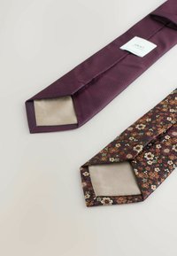 Du šalikai guli šalia: tamsiai raudonas tekstūruotas šalikas su vientisu smėlio spalvos užpildu ir tamsus gėlių rašto šalikas su smėlio spalvos užpildu ir mažais akcentais.