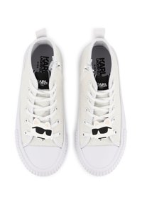 Baskets blanches avec une finition scintillante, dotées de lacets blancs, de semelles en caoutchouc et d'un charm décoratif en forme de chat portant des lunettes de soleil sur le lacet.