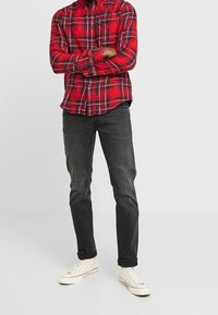 Camicia a quadri rossa e blu, bottoni, maniche lunghe, orlo curvo. Jeanz neri, slim fit, abbinati a sneakers bianche. Design semplice senza loghi visibili.