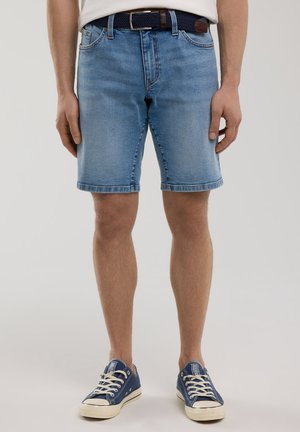 Shorts en denim bleu clair, avec une coupe droite, un ourlet effiloché et cinq poches. Associés à des baskets en toile navy.