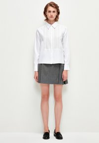 Camisa blanca con detalle de pliegues verticales, combinada con una falda gris con pliegues. La modelo lleva mocasines negros; diseño minimalista, sin patrones.