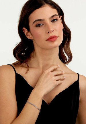 Silberne Armbanduhr mit einem zarten Kettendesign, die am Handgelenk getragen wird und die miteinander verbundenen Glieder sowie die glatte Textur auf der Haut hervorhebt.