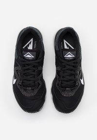 Baskets de trail Nike noires avec une tige en mesh texturé, des accents réfléchissants, et un logo swoosh blanc sur les côtés. Semelle extérieure en caoutchouc pour une meilleure traction.