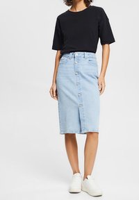 Vaaleansininen farkumidi-hame, jossa on edessä nappisulku, vyölenkit ja sivutaskut, yhdistettynä mustaan lyhythihaiseen t-paitaan ja valkoisiin tennareihin.