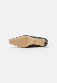 Chaussure plate noire avec un dessus texturé présentant un motif crocodile. Semelle en caoutchouc beige lisse avec des lignes de traction et un détail de logo.