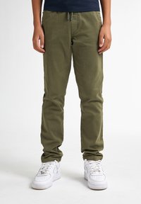 Olijfgroene katoenen broek met een slim fit, een elastische tailleband met trekkoord en zijzakken. Gecombineerd met witte sneakers.