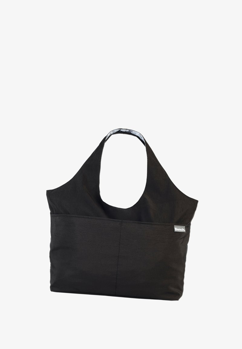 Schwarze Stofftragetasche mit einem breiten Schultergurt, großem Hauptfach und einer Fronttasche. Mit kleinem "Bench."-Logo.