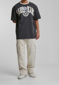 Black graphic t-shirt with cream lettering and logo, paired with light beige cargo pants featuring side pockets and snaps at the ankle.