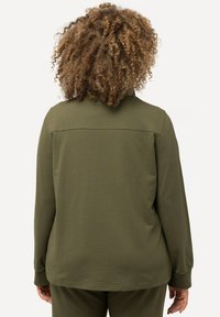 Camiseta de manga larga en verde oliva, hecha de una tela suave, con un cuello redondo y una costura en la parte superior de la espalda. Corte simple y relajado.