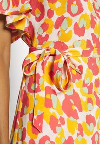 Blommig klänning med rosa, gula och gröna mönster. Har volangärmar och ett tygband i midjan, tillverkad av strukturerat material.