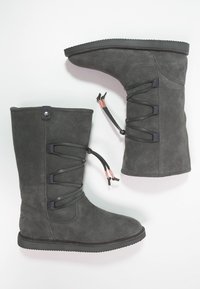 Bottes en suède gris de hauteur mi-mollet, à bout rond et semelle en caoutchouc noir. Elles disposent de lacets noirs et d'un accent en matériel décoratif.