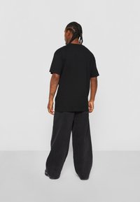 Sort bomulds t-shirt med afslappet pasform, korte ærmer og rund halsudskæring, parret med løse sorte denimbukser.