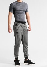 Graues Sportshirt mit strukturiertem Muster und kurzen Ärmeln, kombiniert mit grauen Jogginghosen mit Taschen und schwarzen Akzenten, getragen mit schwarzen Sportschuhen.