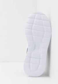 Zool van een sneaker, met een gestructureerd wit rubber materiaal, geometrisch loopvlakpatroon en een logo-afdruk in het midden.
