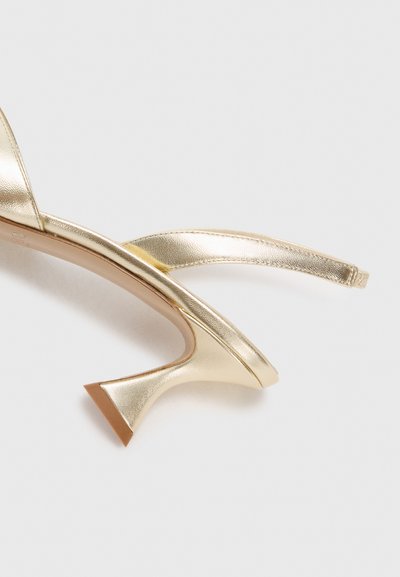 Gold metallic high-heeled shoe with a slingback design, pointed toe, and a sculpted heel. Smooth texture and minimalistic style.