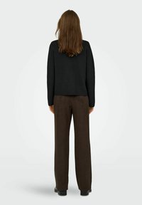 Schwarzer kurzer Pullover und braune weite Hose. Der Pullover hat eine strukturierte Oberfläche; die Hose hat eine glatte, wildlederartige Textur.