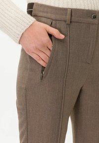 Brązowe spodnie o dopasowanym kroju z estrukturalnego materiału. Posiadają boczną kieszeń na zamek, klasyczne zapięcie na guzik oraz fason slim fit.