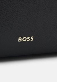 Surface en cuir noir texturé avec de petites lettres métalliques dorées formant le mot "BOSS", centrées près du bord inférieur.
