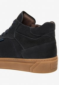 Sneaker alta in suede blu navy con suola in gomma color cuoio, colletto imbottito e rivestimento in pelle marrone a contrasto. Presenta dettagli di cucitura sottili.