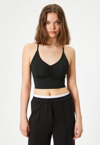 Top corto negro con tirantes ajustables de espagueti, parte frontal fruncida y un diseño ajustado. Combinado con pantalones de chándal negros que tienen una cinturilla elástica blanca.