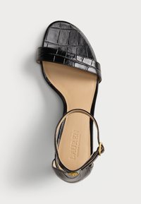Μαύρη δερμάτινη σανδάλι επίπεδου τακουνιού με υφάνσεις κροκοδείλου, μία μπροστινή ταινία, ταινία αστραγάλου με χρυσό κούμπωμα και μπεζ σόλα με ανάγλυφη σήμανση της μάρκας.