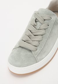 Sneaker in suede grigio chiaro con superficie texturizzata, lacci intrecciati, suola in gomma bianca e design pulito con accenti minimi.