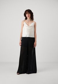 Silke cami med drapert halsutringning i off-white, parret med højtaljede sorte plisserede bukser i vid ben-silhuet.