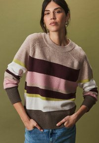 Pull en tricot avec des rayures horizontales en beige, rose, marron foncé, blanc et vert. Col rond et détails de poignets et d'ourlet côtelés.