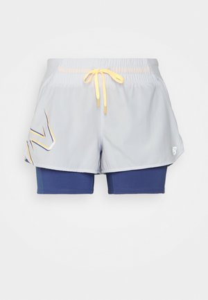 Vaaleanharmaat urheilushortsit, joissa on keltainen nauha ja siniset tiukat sisäshortsit, joissa on tyylitelty logo vasemmalla ulkokerroksella.