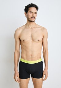 Black boxer briefs with a neon yellow waistband featuring "PUMA" logo. Fabric is soft, stretchy, and form-fitting, suitable for daily wear.