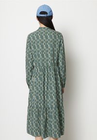 Abito a maniche lunghe in tessuto verde con un motivo a righe verticali. Presenta un corpetto arricciato e una gonna a strati. Abbinato a un cappellino azzurro chiaro.