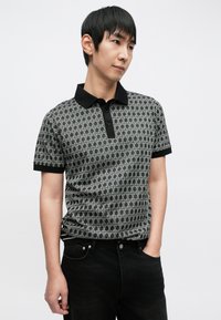Polo de manga curta em preto e branco com padrão geométrico, gola preta e três botões na pala. Design ajustado.