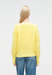 Κίτρινο πλεκτό που λόβερ με άνετη εφαρμογή, ριμπ μανσέτες και τελείωμα. Συνδυασμένο με μπλε τζιν ψηλόμεσο. Υφή από ελαφρύ ύφασμα.