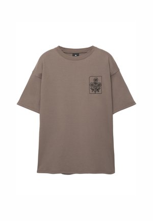 Barna, oversize póló, puha pamutból készült, kis fekete virágmintás hímzéssel a bal oldali mellzseben.