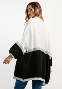 Przesadnie duży kardigan dzianinowy w czarno-biało-szarym wzorze kolorystycznym. Posiada długie rękawy oraz luźny krój, wykonany z teksturowanej mieszanki wełny.