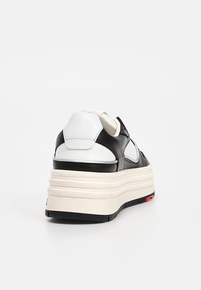 Sneaker in pelle bianca e nera con una suola platform spessa color crema, caratterizzata da accenti curvi e una finitura testurizzata sulla tomaia. Dettaglio rosso sulla suola.