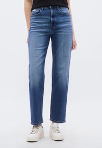 Μπλε τζιν τζιν με ευθεία γραμμή, ελαφρώς ξεβαμμένο πλύσιμο και ψηλή μέση. Συνδυασμένο με λευκά αθλητικά παπούτσια.