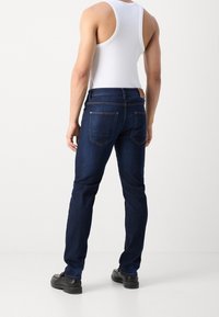 Mörkblå jeans i slim fit med bakfickor och kontrasterande sömmar. Bärs med en vit linne och svarta skor.