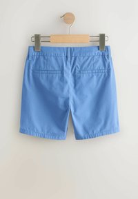 Pantaloncini di cotone blu con una texture liscia, caratterizzati da un taglio dritto, tasche posteriori e una vita standard. Appesi a una molletta di legno.