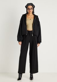 Crna zip-up hoodie, bež krojena majica bez rukava, crne široke hlače i crne čizme na petu. Dodatno je ukrašena sa šarenim maramom i naočalama za sunce.