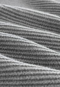 Grå stickad tyg med strukturerade vågor och växlande ljusa och mörka ränder, som visar en mjuk och mysig känsla.