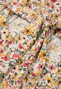 Tkanina w kwiatowy print z mieszanką czerwonych, różowych, żółtych i zielonych kwiatów na jasnym tle, z miękkim, teksturowanym zwisaniem.